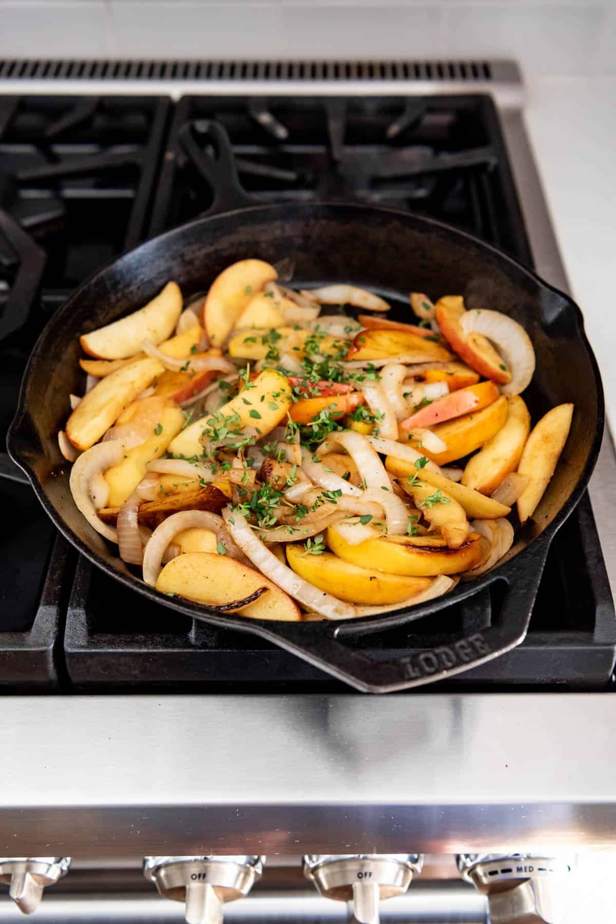 An image of sauteed apples, onions, and thyme in a cast iron skillet on the stove for a chicken skillet meal with apples.