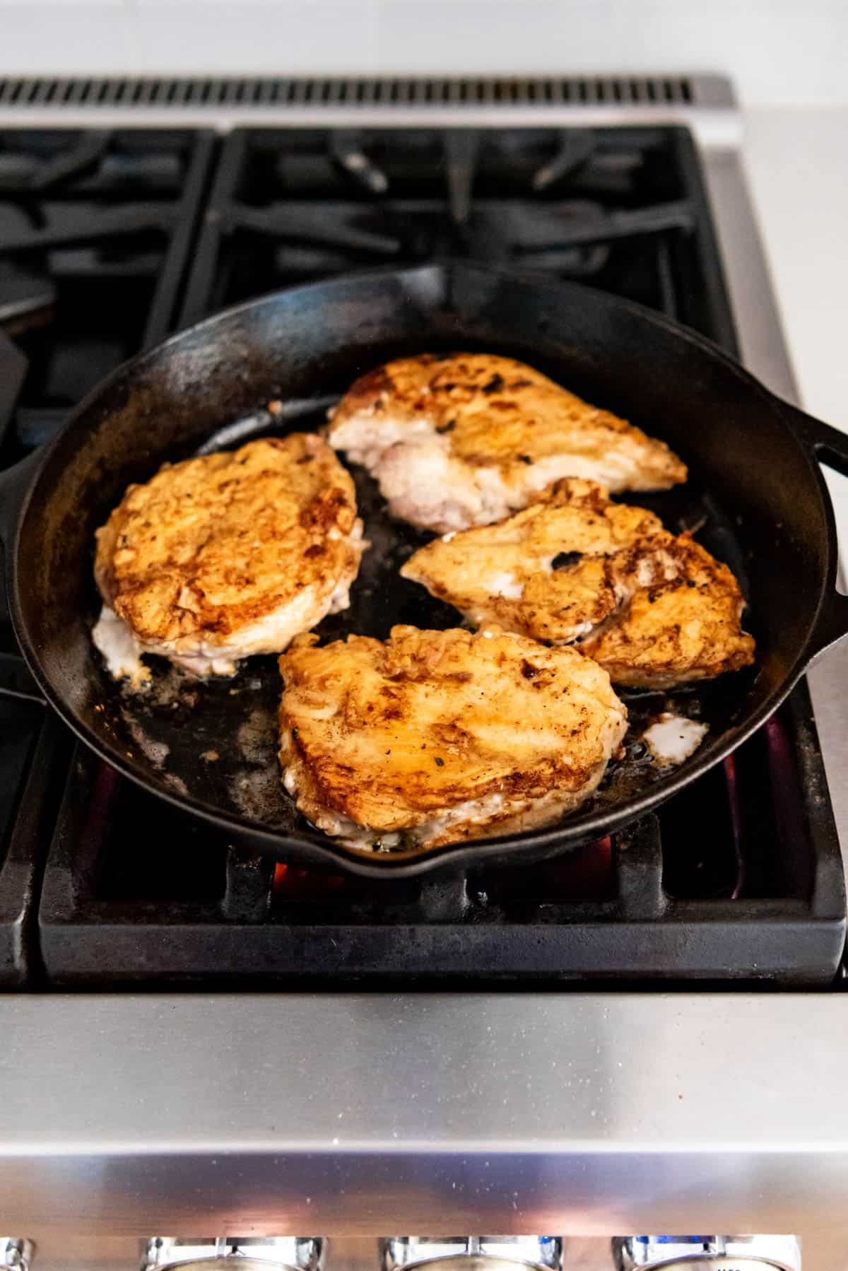 An image of crispy chicken thighs in a cast iron skillet on the stove top.