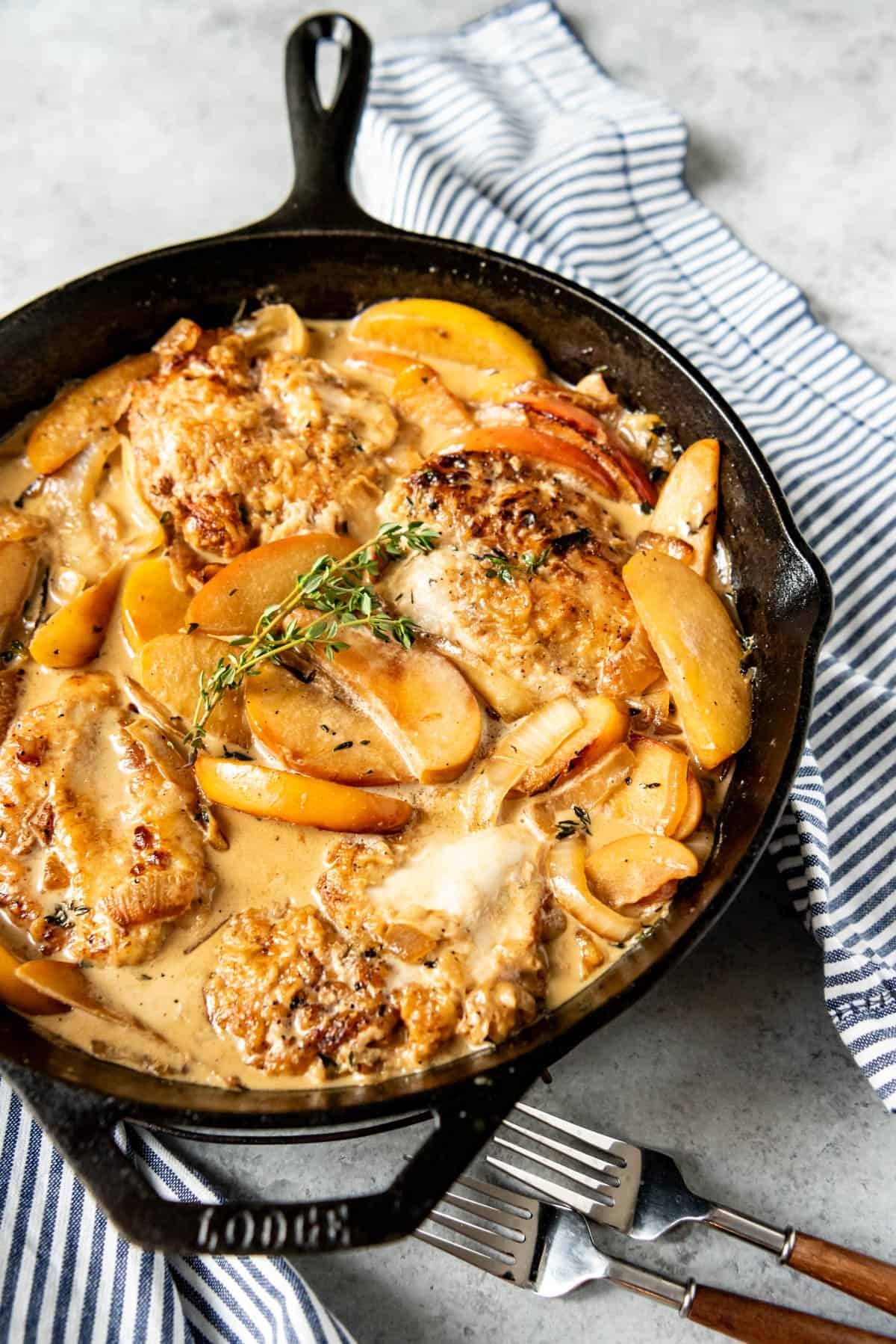 a skillet full of creamy apple cider chicken and topped with fresh herbs for garnish