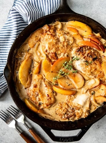 apple cider chicken in a skillet with apple slices