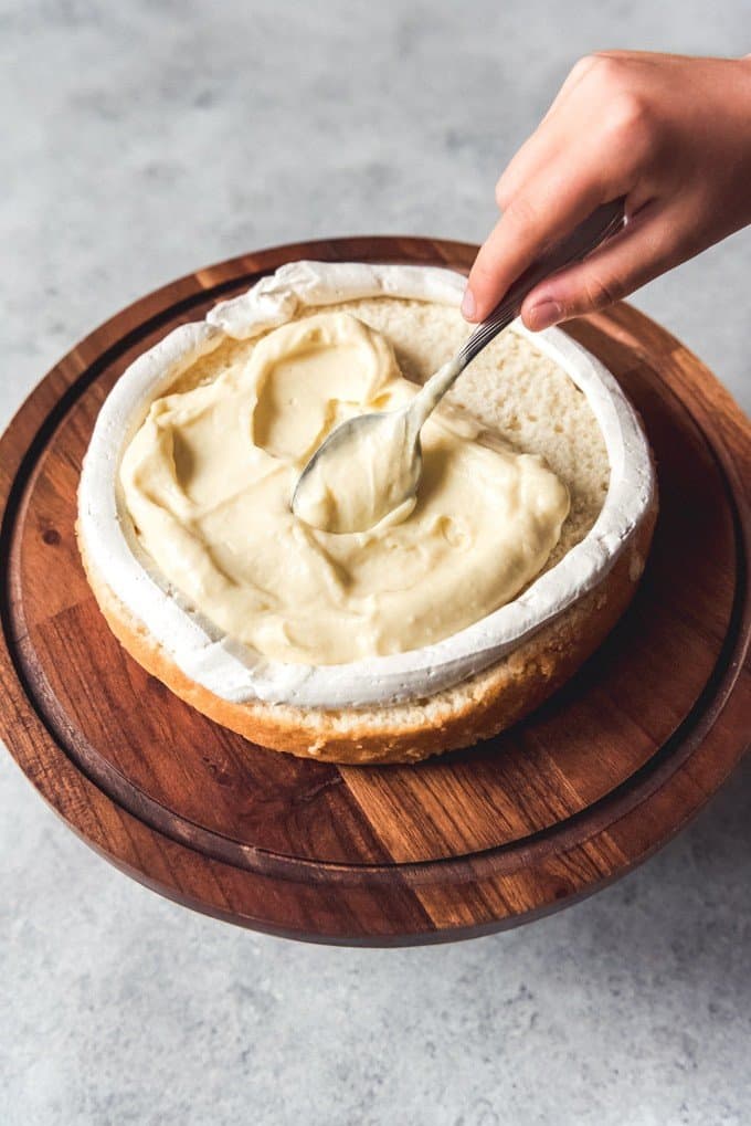 An image of French pastry cream being spread onto a layer of white cake with a ring of Swiss Meringue Buttercream piped around it to fill a burnt almond cake.