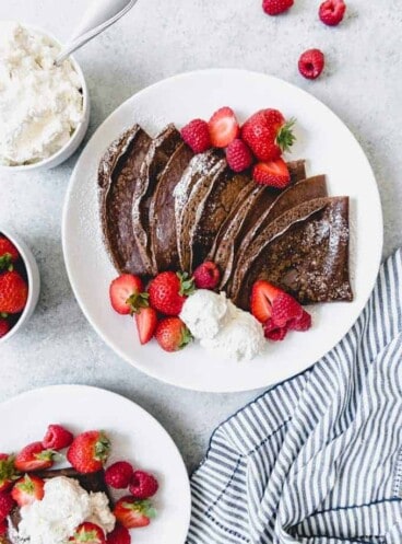 white plates topped with chocolate crepes, cream and berries