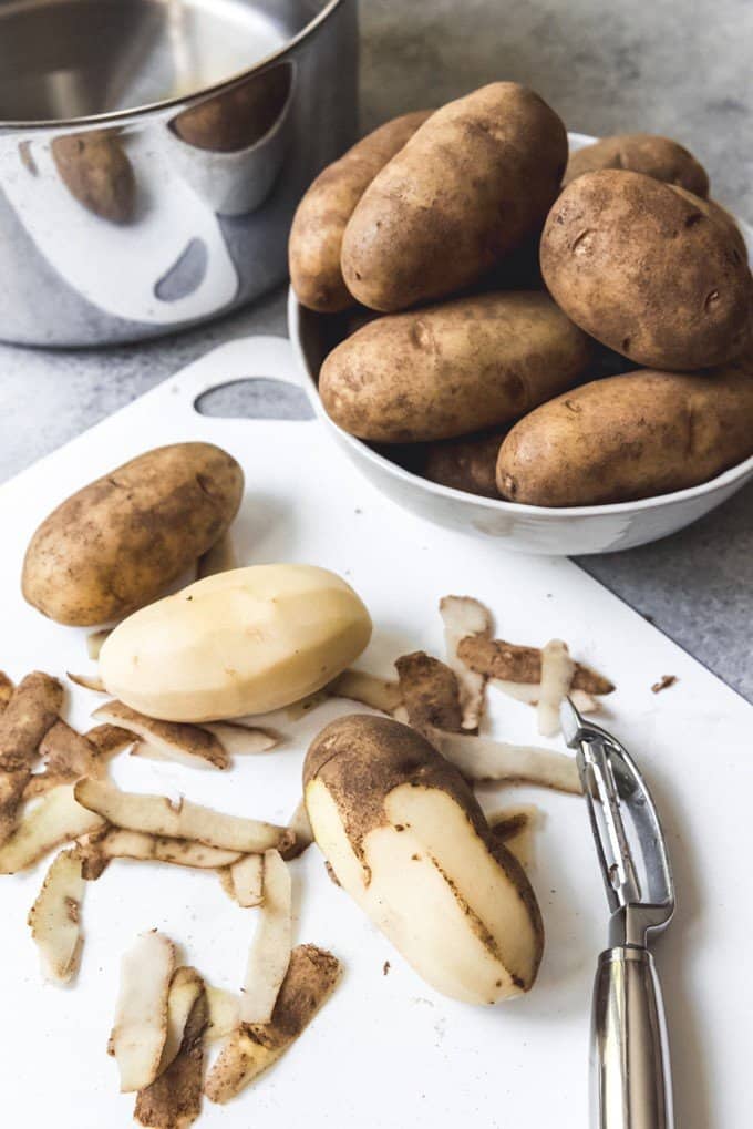 An image of peeled Russet potatoes on a cutting board and unpeeled Russet potatoes in a bowl.
