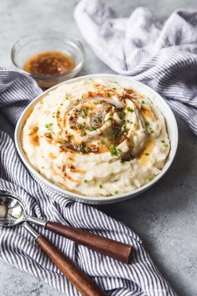 A big bowl of creamy mashed potatoes for Thanksgiving dinner with browned butter drizzled over top.