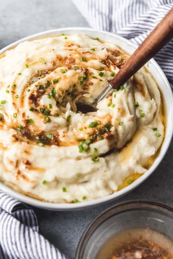 An image of a serving spoon with a wooden handle in a bowl of garlic browned butter mashed potatoes for Thanksgiving.
