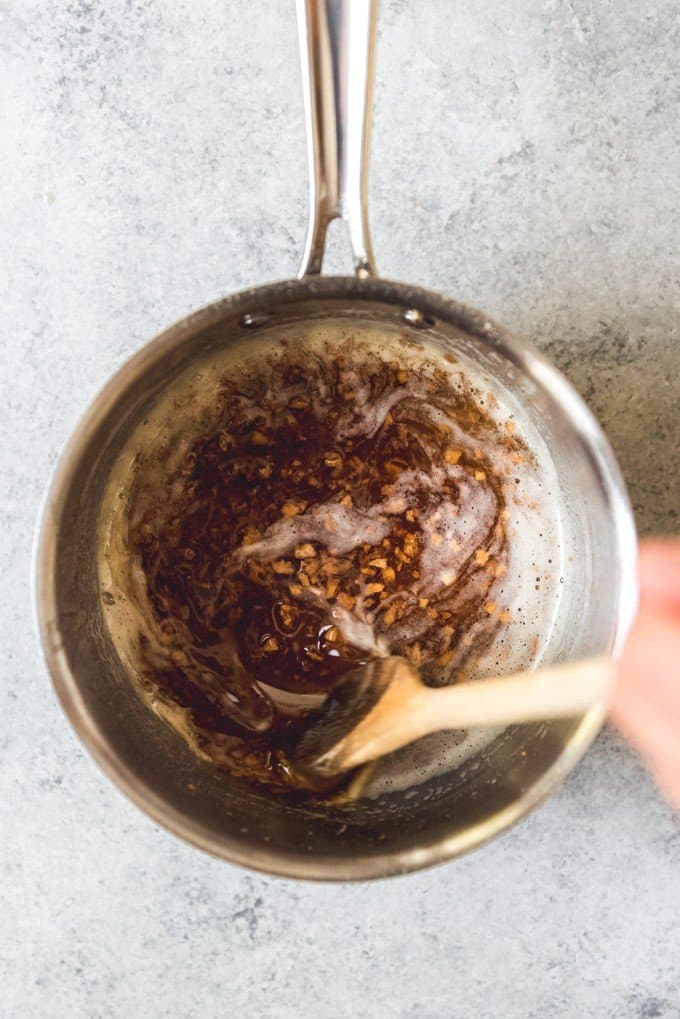An image showing how to make brown butter with garlic in it showing a hand stirring a wooden spoon in a pan.