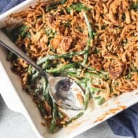 a close up of a white baking dish with green bean casserole and a serving spoon inside