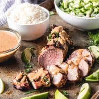 Grilled Thai Pork Tenderloin on a tray with a bowl of rice and other ingredients to the side