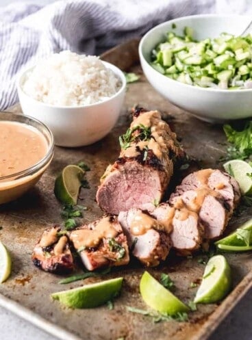 Grilled Thai Pork Tenderloin on a tray with a bowl of rice and other ingredients to the side