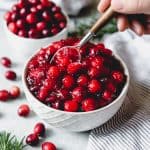 a hand sticking a spoon into a bowl of homemade cranberry sauce