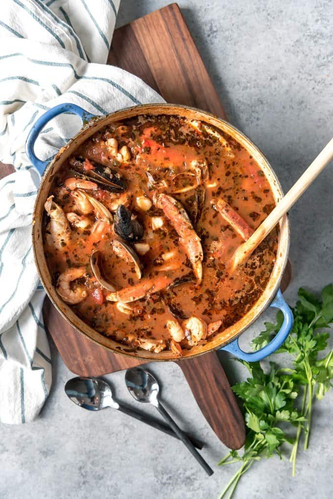 A large blue pot full of seafood stew resting on a wooden cutting board