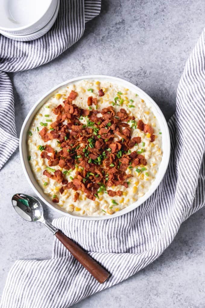 An image of a bowl of cream style corn with bacon and chives on top.