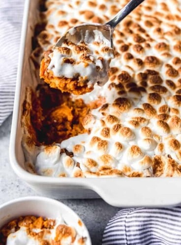 sweet potato casserole with marshmallows in a white baking dish with a spoon scooping some out of the pan