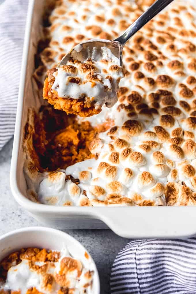 sweet potato casserole with marshmallows in a white baking dish with a spoon scooping some out of the pan