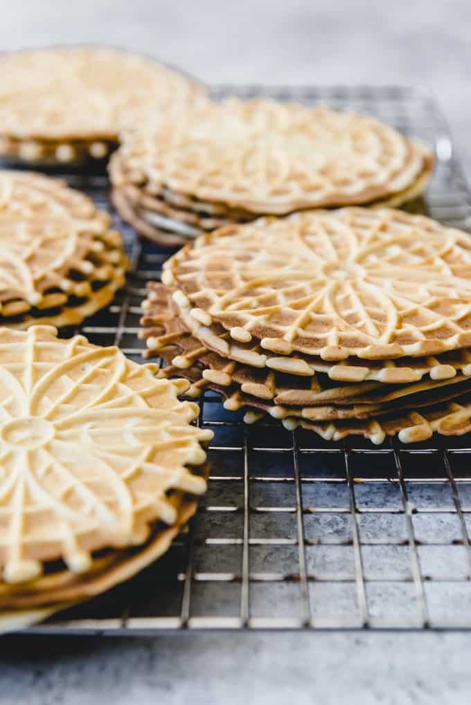 An image of classic anise pizzelles stacked on a wire rack.