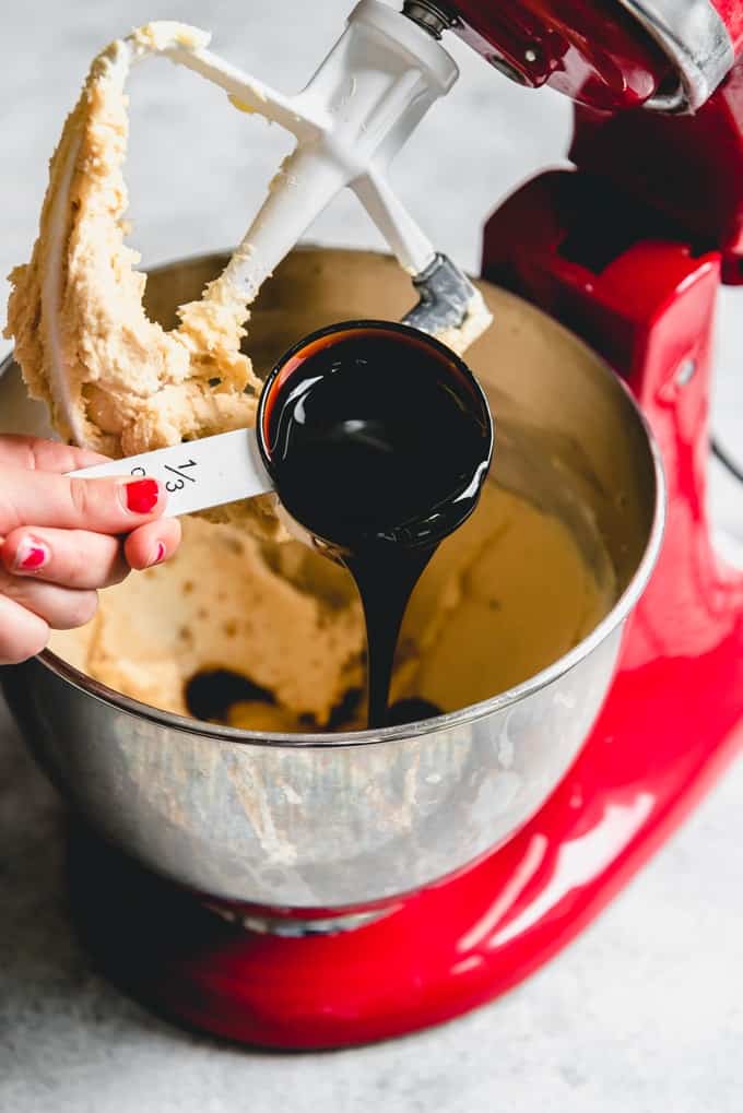 An image of molasses being poured into creamed butter in a mixer to make soft molasses cookie dough.