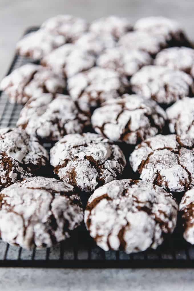 An image of chocolate crinkle cookies covered in powdered sugar and cooling on a wire rack.
