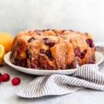 A loaf of cranberry orange monkey bread on a white plate next to a striped linen napkin.