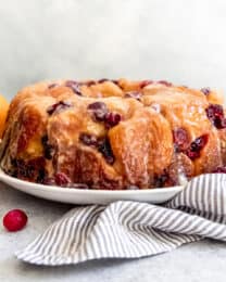 A loaf of cranberry orange monkey bread on a white plate next to a striped linen napkin.