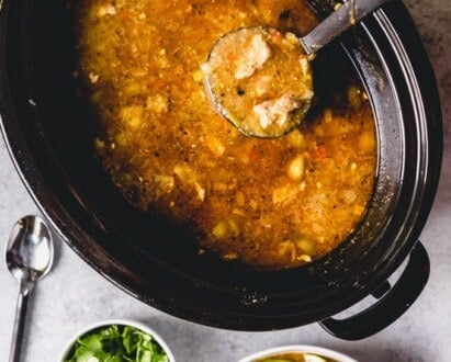 scooping pork green chili out of a slow cooker with a ladel