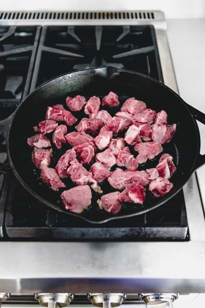 cooking cut pork chunks on a stove in a cast iron skillet