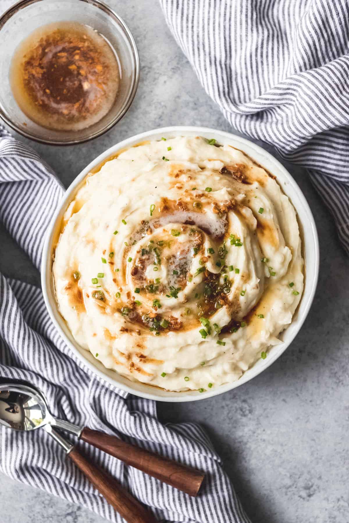 An image of a large bowl of buttery mashed potatoes for Thanksgiving or Christmas dinner with extra browned butter on the side.