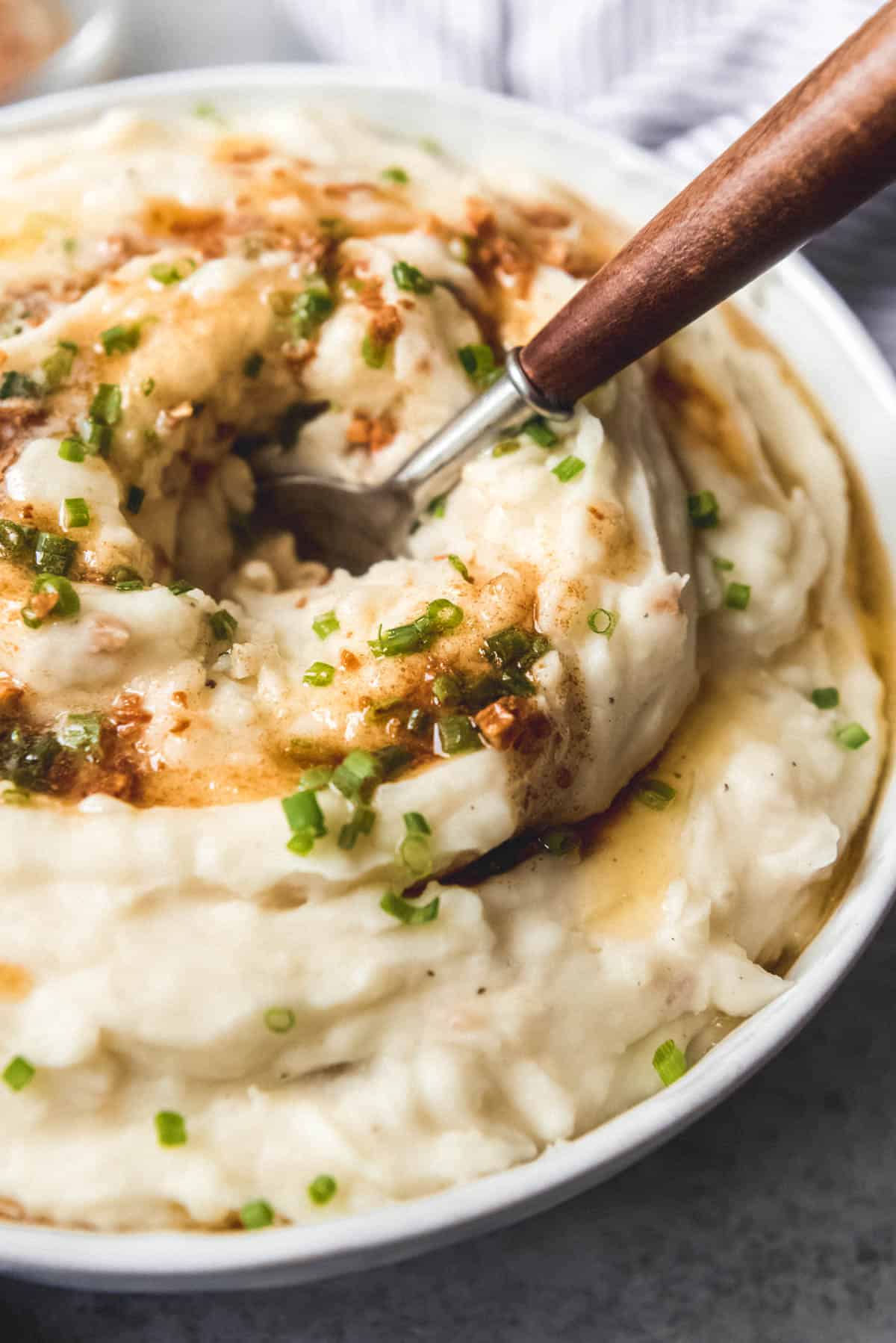 A close-up image of mashed potatoes topped with brown butter sauce and chopped chives.