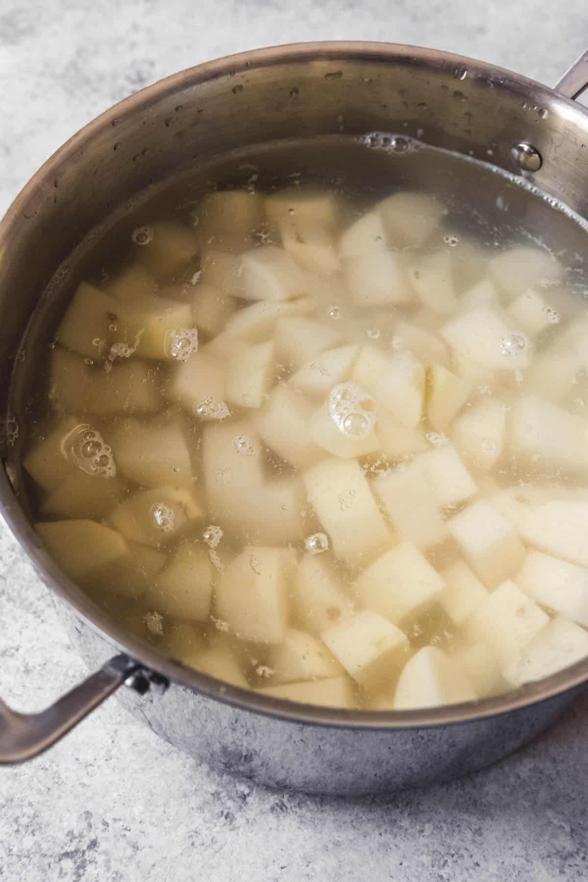 An image of Russet potatoes chopped and placed n a pot of cold, salted water to cook for a mashed potatoes recipe.