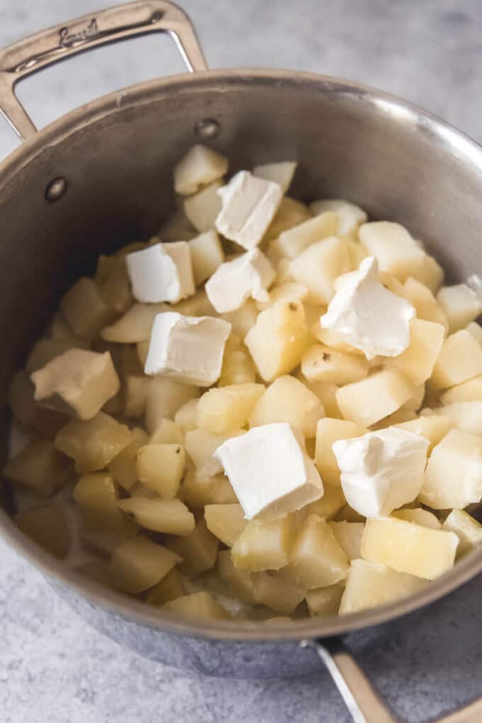 Adding cubed cream cheese to boiled potatoes.