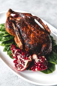 honey roasted duck on a white platter with spinach and pomegranate