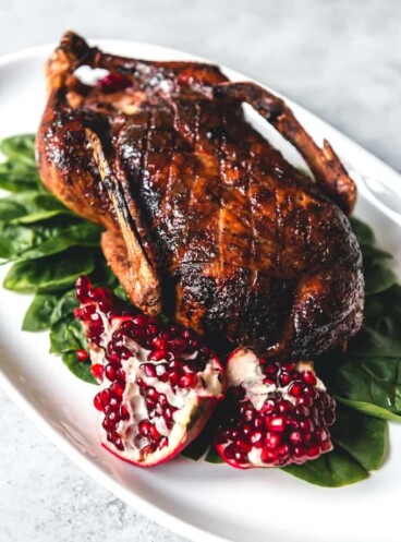 honey roasted duck on a white platter with spinach and pomegranate