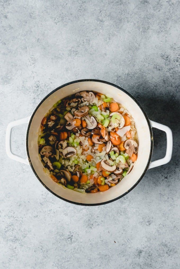 An image of a pot full of sauteed onions, mushrooms, carrots, celery, and garlic for making creamy turkey wild rice soup.