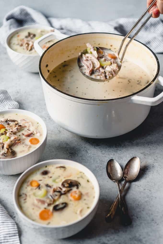 An image of a ladle-full of creamy turkey wild rice soup over a large pot of soup.