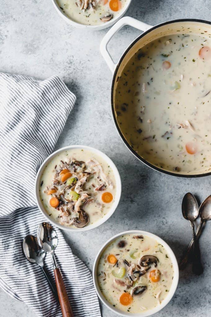 Two bowls of creamy turkey soup with wild rice next to a large pot of the soup.