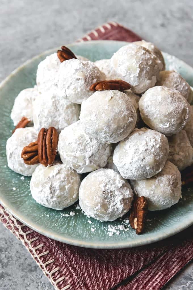 whole pecans in a pile of mexican wedding cookies on a plate