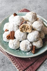 a plate filled with mexican wedding cookies and scattered whole pecans