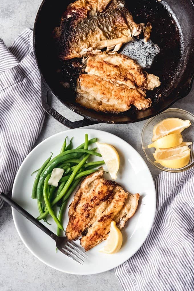 trout fillets in a cast iron skillet and one on a plate with lemon wedges and green beans