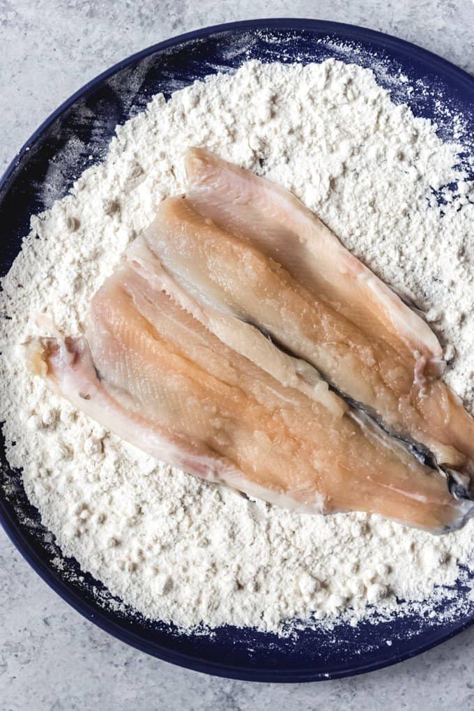 An image of a butterflied rainbow trout being lightly coated in flour.