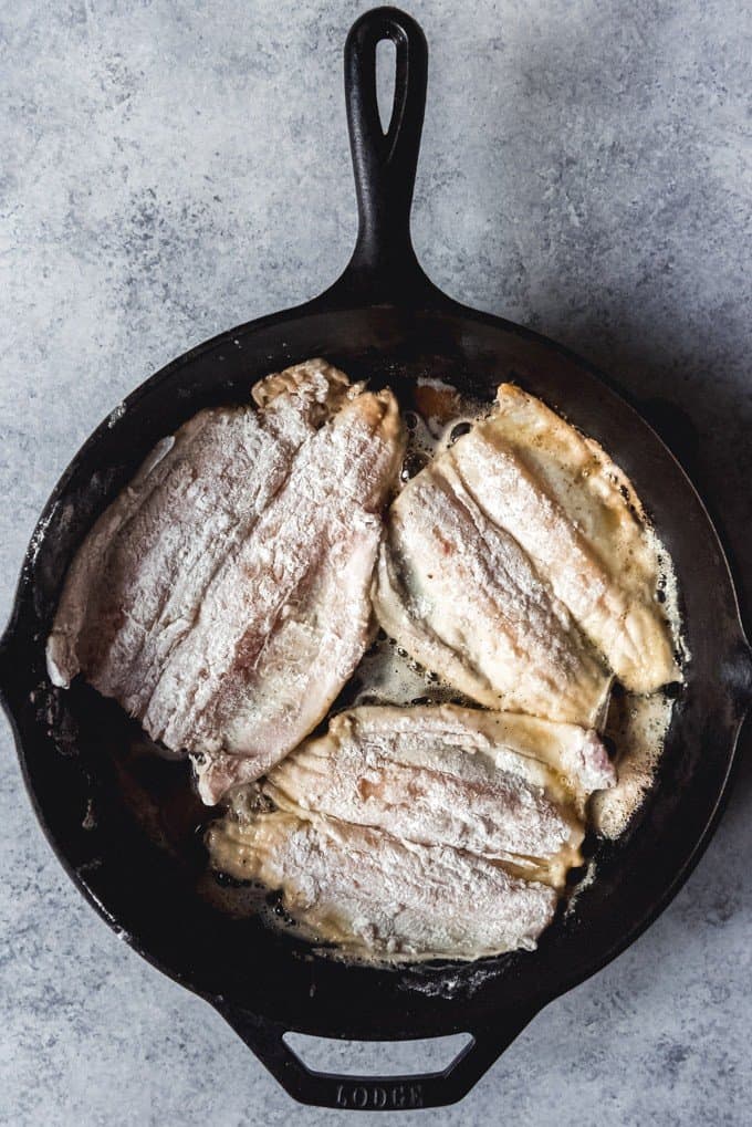An image of flour-coated fish being fried in a cast iron skillet.