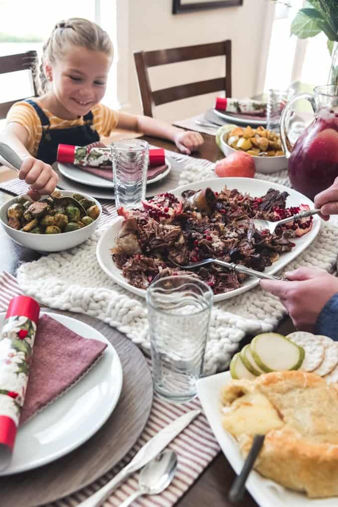 adult hands serving up lamb shoulder with a childs hand serving brussel sprouts at the dinner table