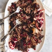 a platter with serving utensils and pomegranate braised lamb shoulder