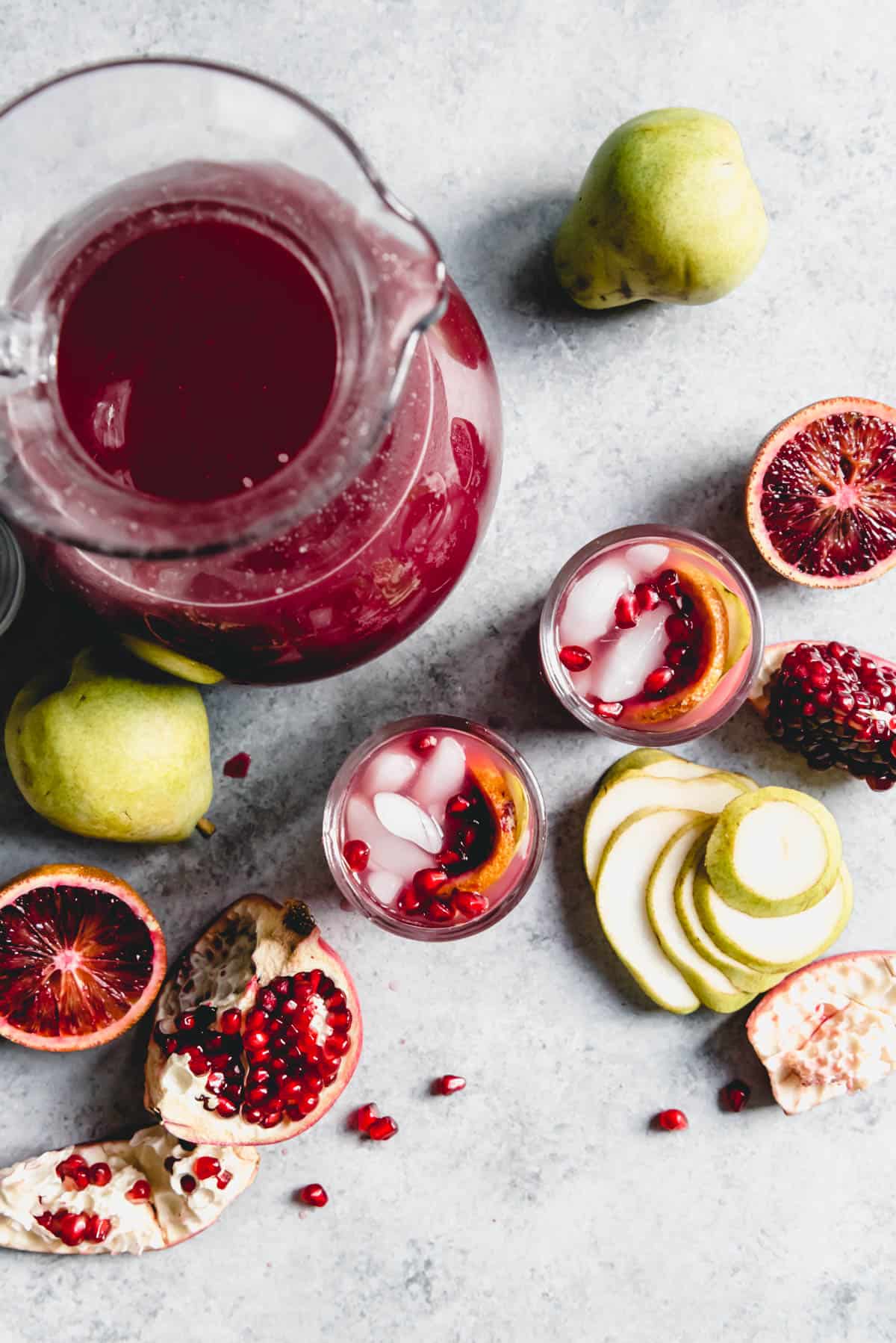 An image of a pitcher of a sparkling fruit punch in a pitcher with a couple of glasses garnished with pears, blood oranges, and pomegranate seeds beside it.