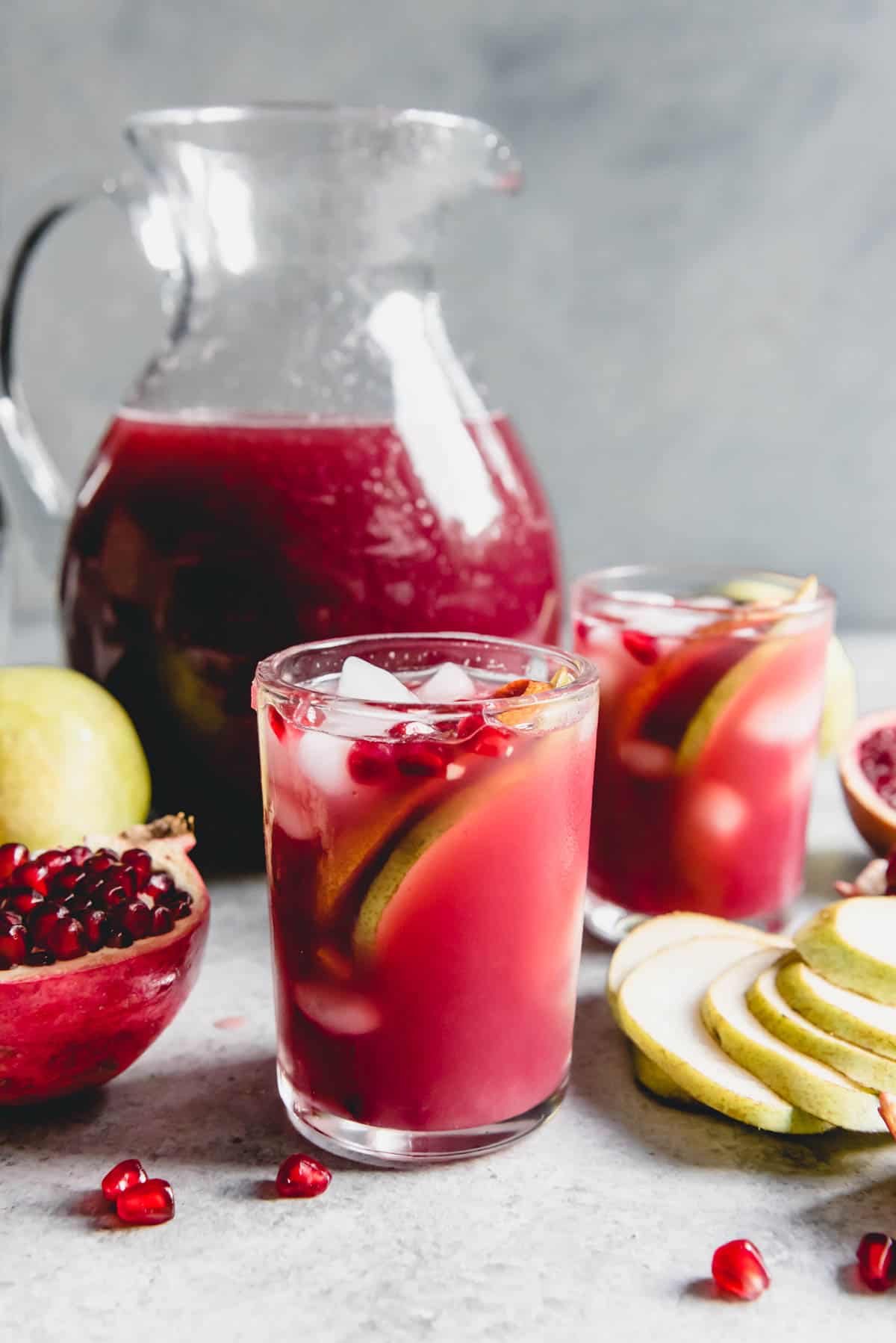 Pomegranate in a Pear Tree Punch in glasses and in a pitcher with fresh fruit scattered around.