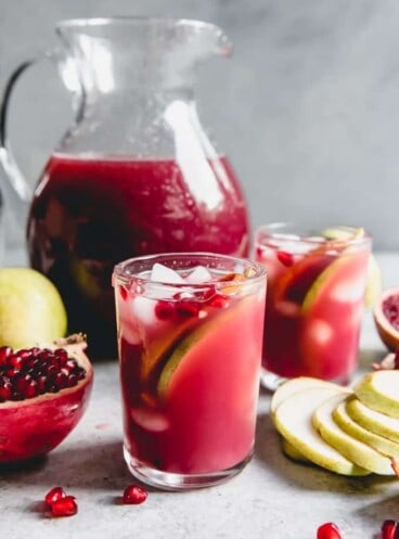 Pomegranate in a Pear Tree Punch in glasses and in a pitcher with fresh fruit scattered around