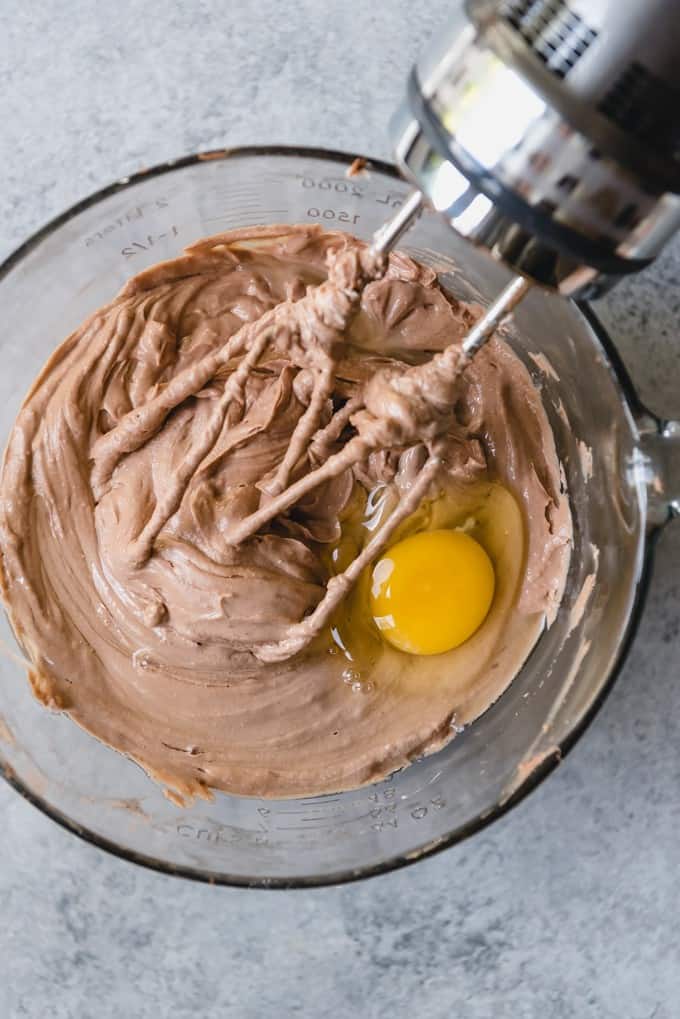 An image of an egg being mixed into chocolate cheesecake batter.
