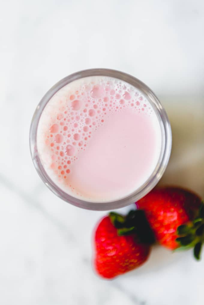 An image of a glass of fresh strawberry milk with strawberries on the side.