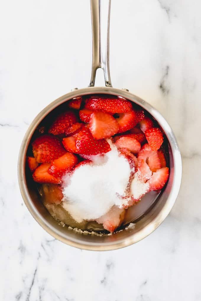 An image of the step-by-step process of making strawberry syrup for strawberry milk by combining fresh strawberries, sugar, and water in a pan to simmer.