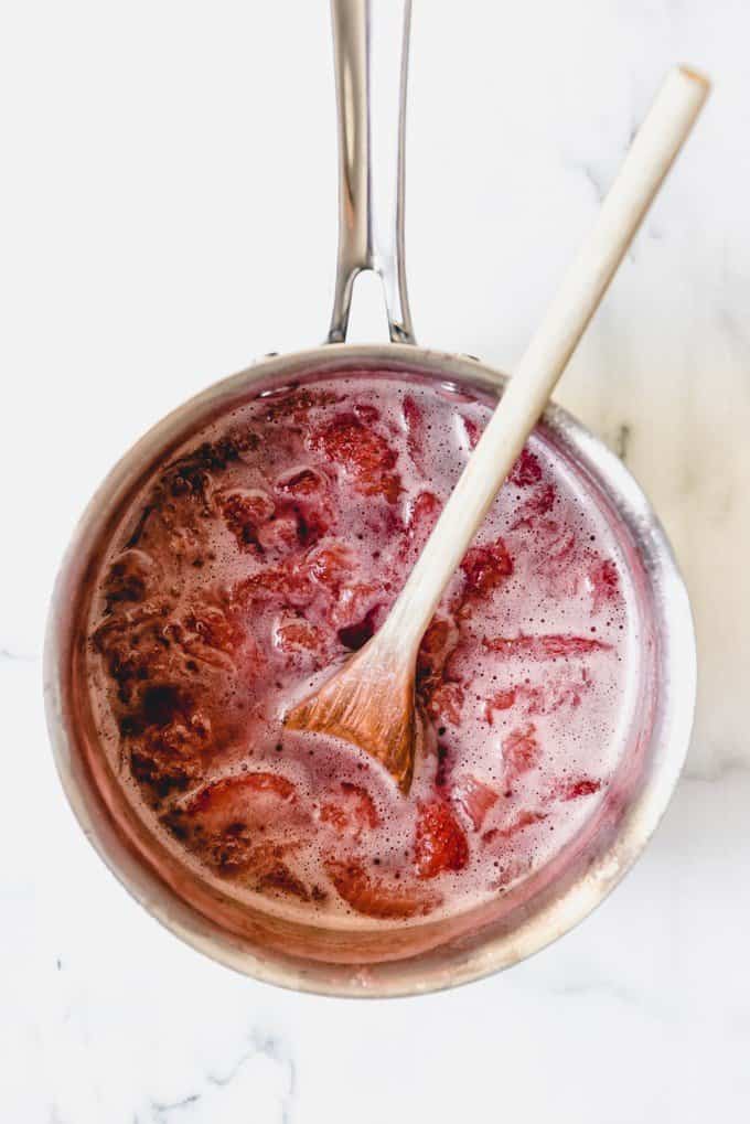 An image of simmer strawberries and sugar ready to be poured through a fine mesh strainer to make strawberry syrup for homemade strawberry milk.
