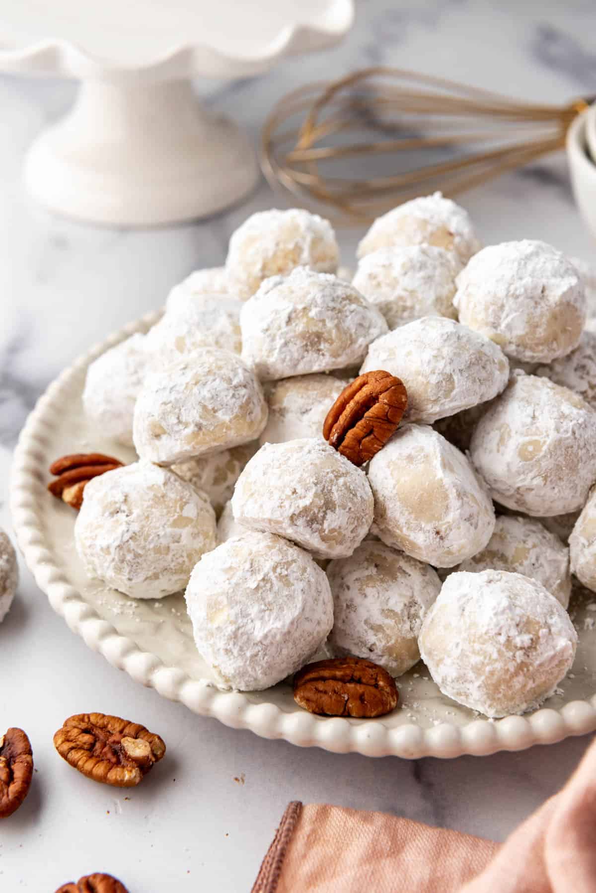 A plate of Mexican wedding cookies covered in powdered sugar with whole pecans scattered around.