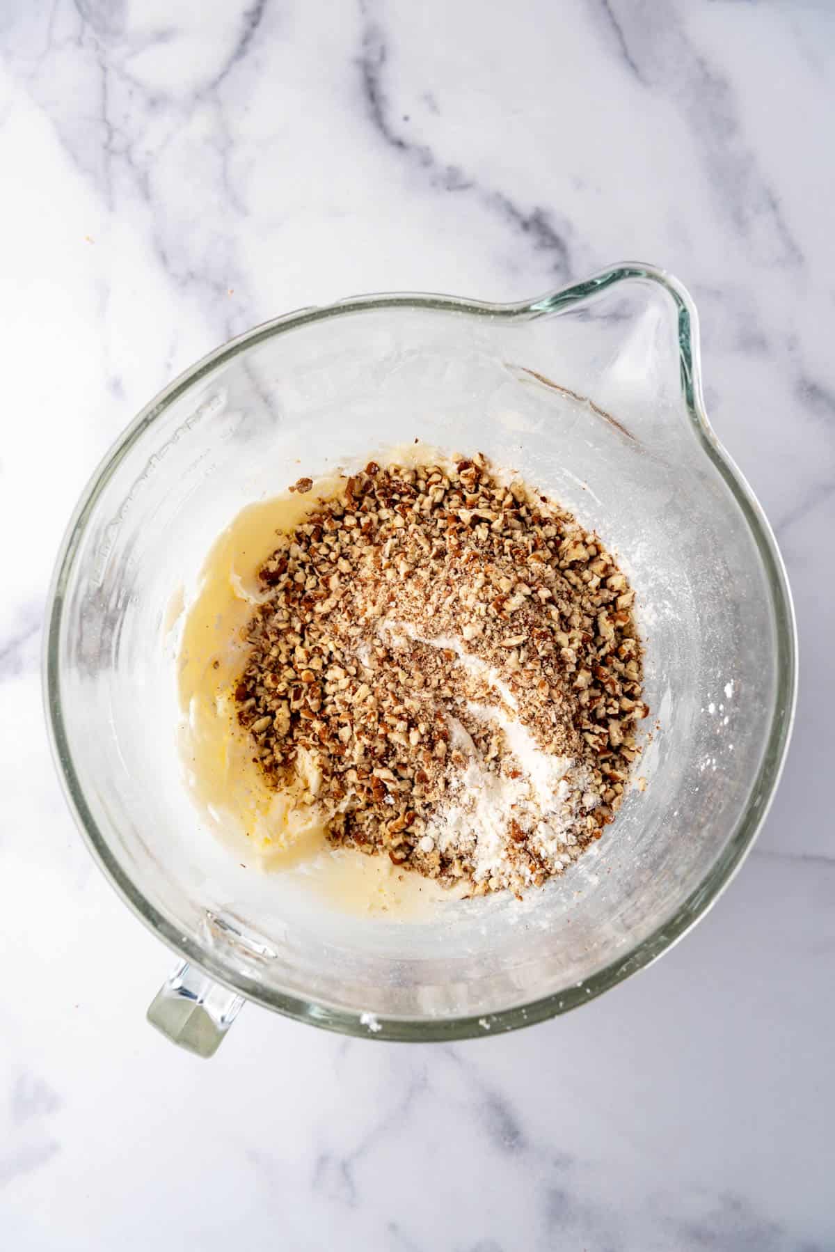 Adding flour and finely chopped pecans to cookie dough in a large glass mixing bowl.